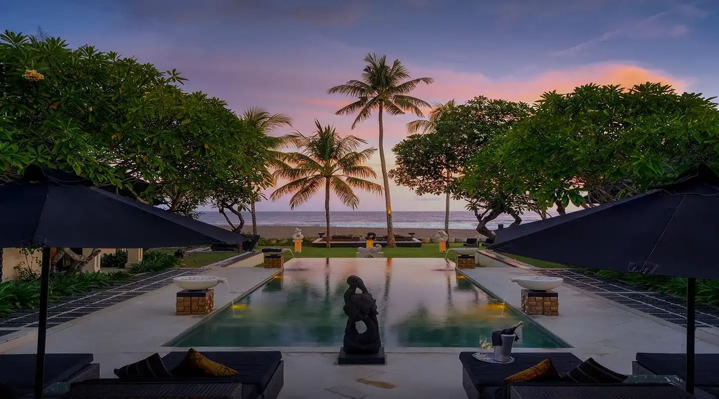Beachfront Bali villa infinity pool at sunset framed by palm trees, champagne set for two